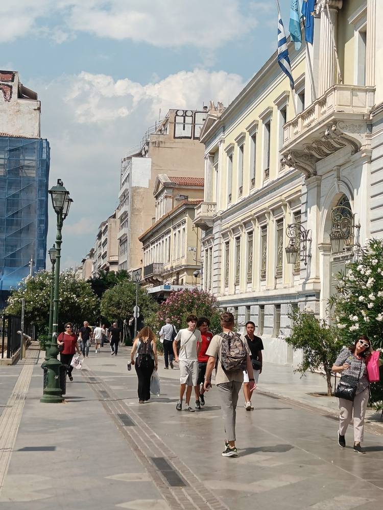 A pedestrian street in central Athens with people walking past neoclassical buildings