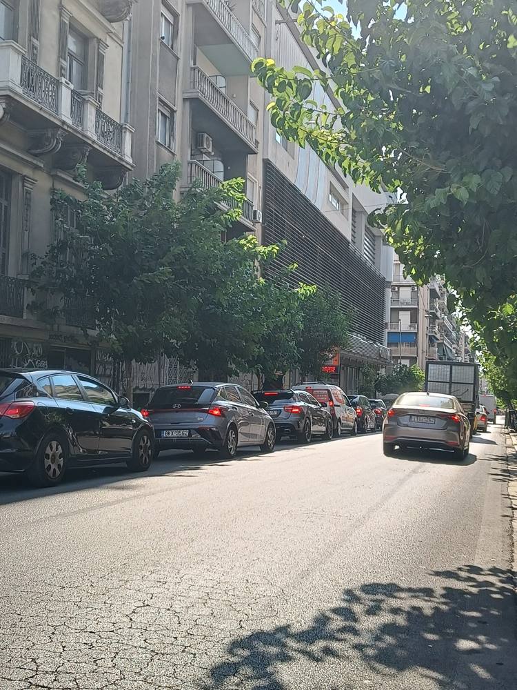A long line of parked cars on a tree-lined Athens street