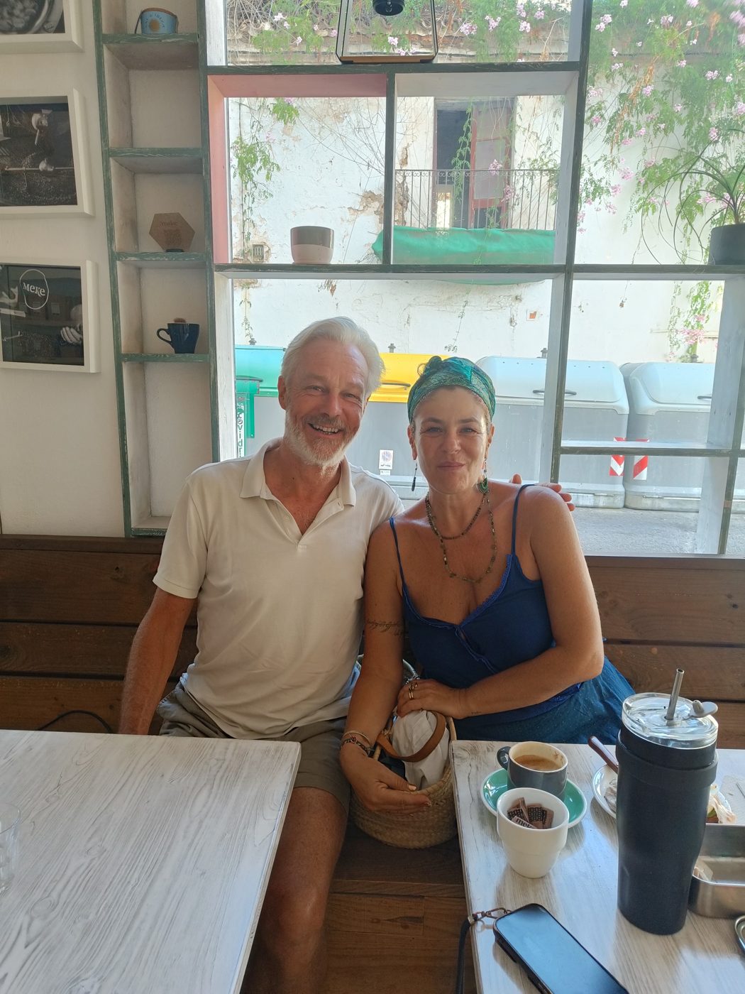 Hans and a woman sitting together at a café table beside a window
