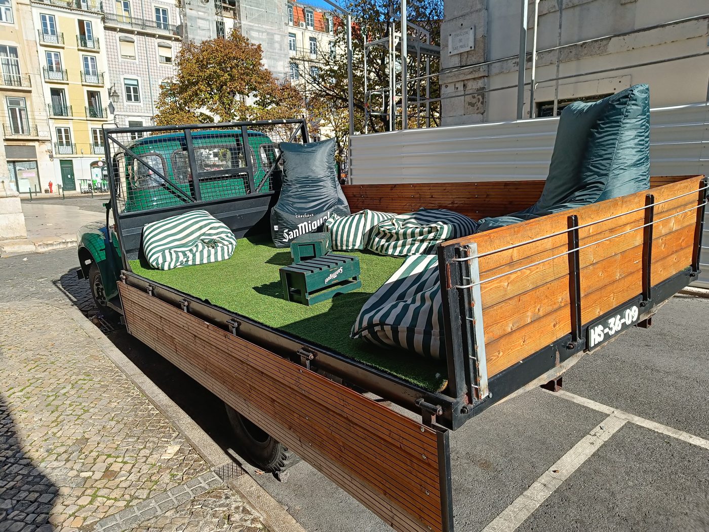 A vintage pickup truck parked in a street bay, its flatbed laid with artificial grass and striped beanbags