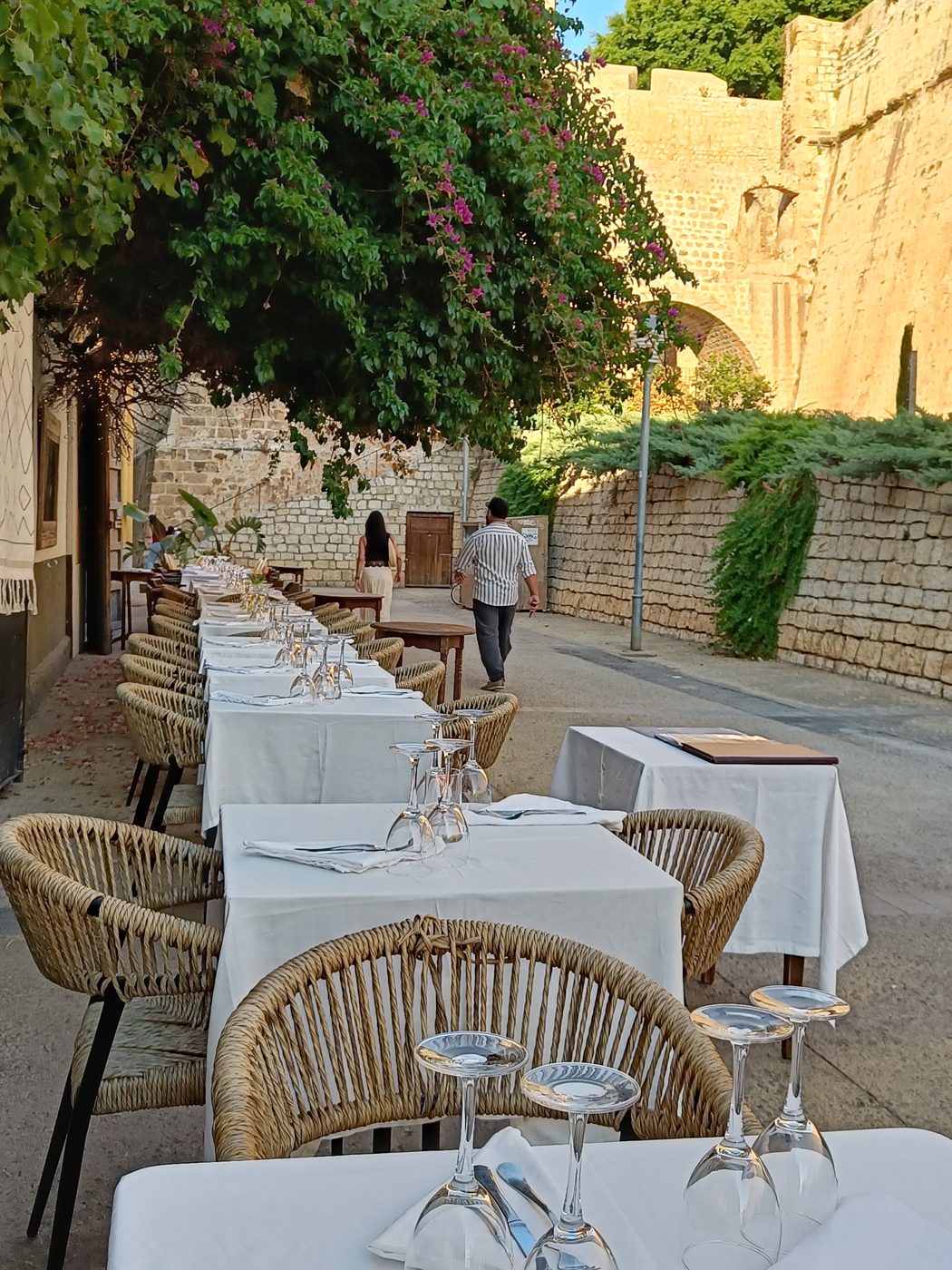 Restaurant tables laid along a narrow street beneath the old stone walls