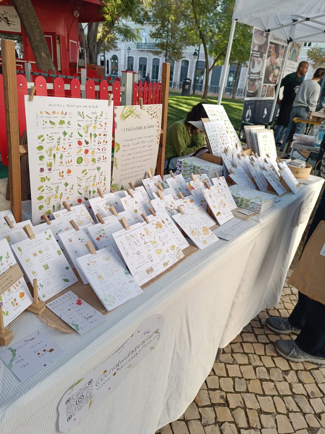 A market stall under a canopy, its table laid out with illustrated cards of food and produce