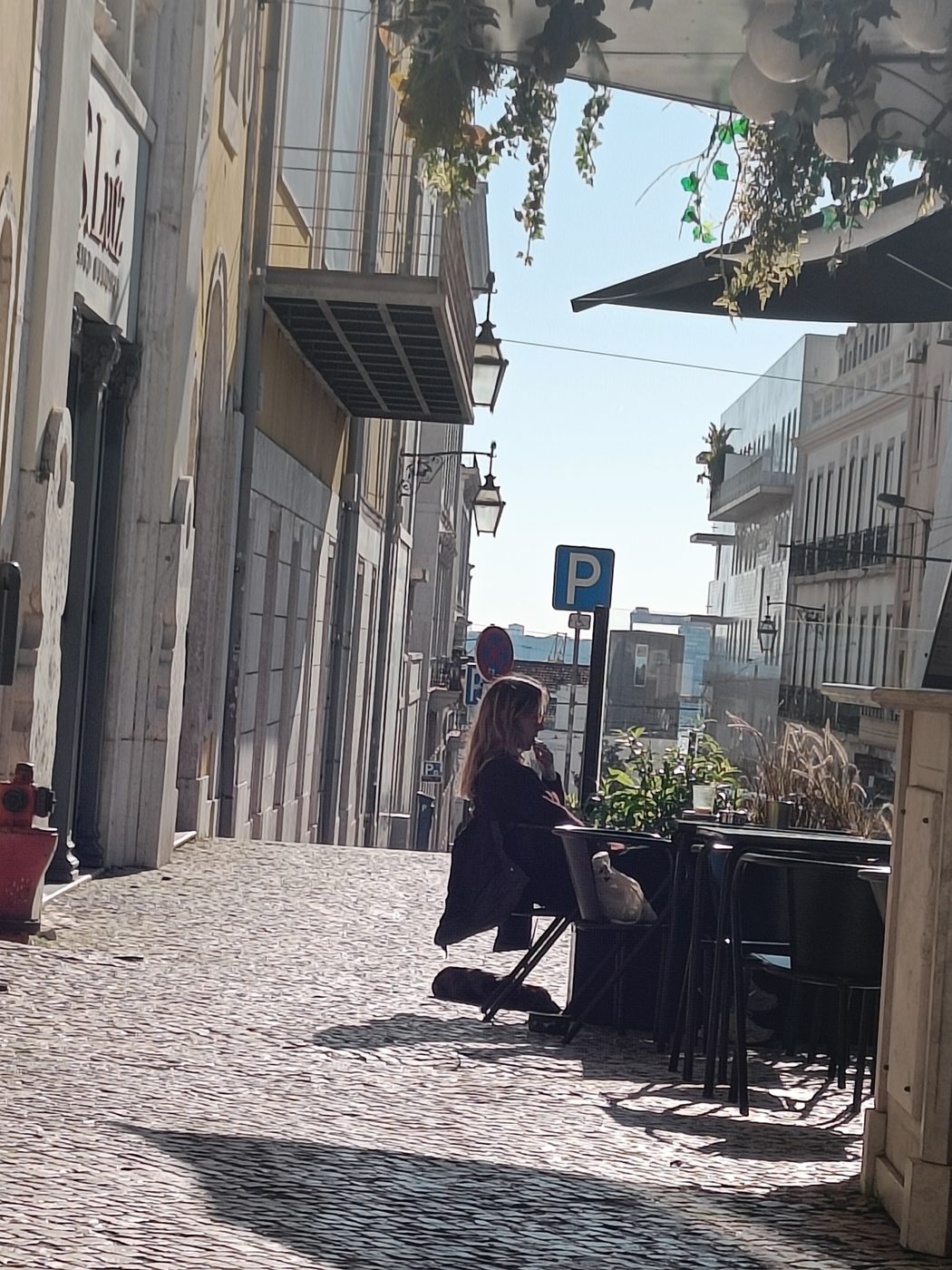 A woman sitting at an outdoor café table on a cobbled Lisbon street